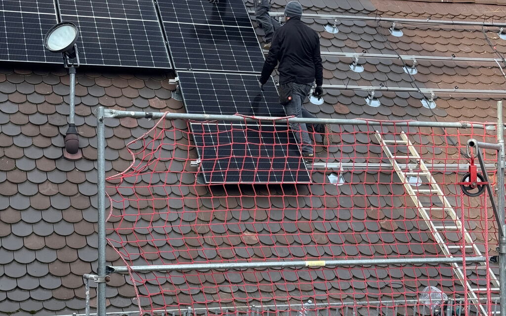 Arbeiter installieren Photovoltaikanlagen auf einem Dach mit Sicherheitsnetz und Gerüst.