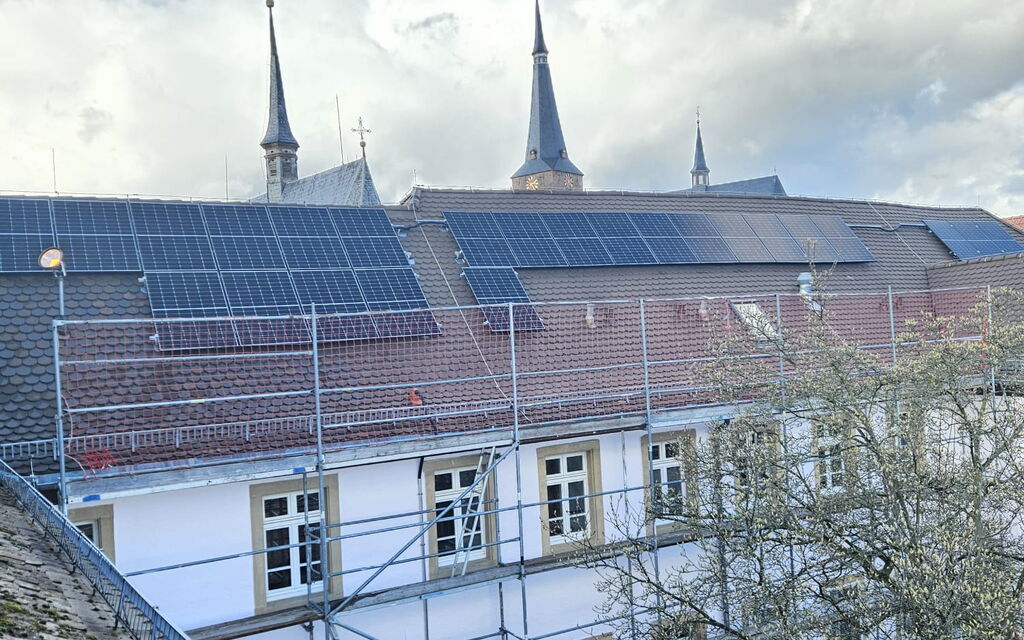 Eine Dachlandschaft mit Photovoltaikanlagen und einem historischen Gebäude unter blauem Himmel.