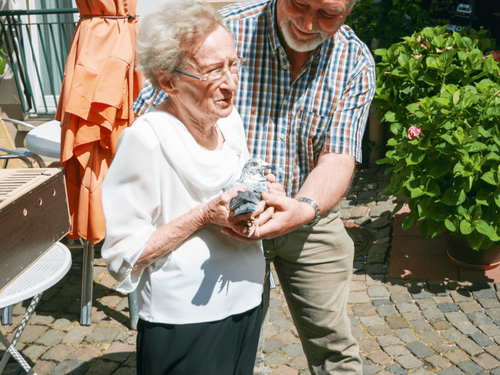 Frau Rittmann-Fischer lächelt, während sie eine Figur zusammen mit einem Mann im Freien hält.