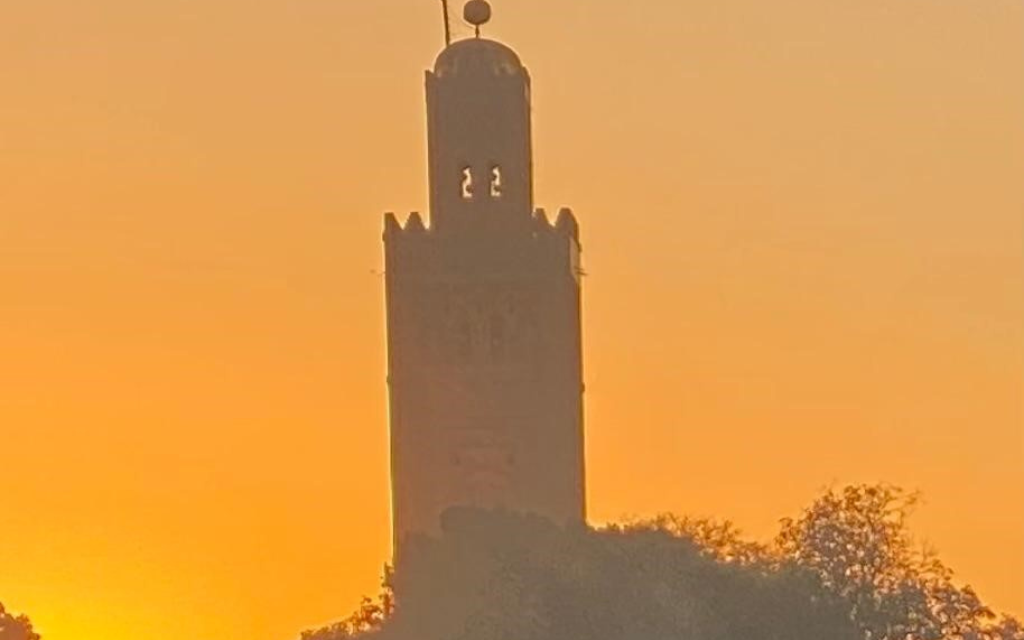 Die Silhouette eines Turms hebt sich gegen den orangefarbenen Sonnenuntergang über Marrakesch ab.