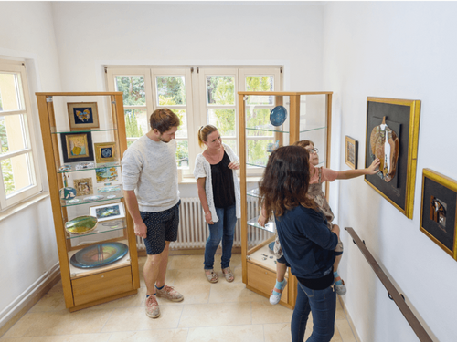 Besucher betrachten beeindruckende Emailarbeiten in einer Galerie mit Ausstellungsstücken und Vitrinen.