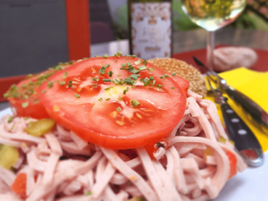 Hausgemachter Wurstsalat mit frischen Tomaten und Zwiebeln, serviert mit einem Glas Wein im Café Ritter von Bohl.