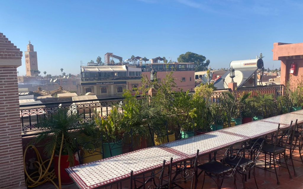 Blick auf den Markt von Marrakesch mit einer Terrasse, Pflanzen und einem Tisch im Vordergrund.