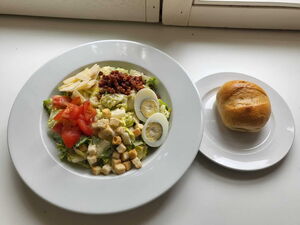 Ein frischer Caesar-Salat mit Eiern und Tomaten, serviert mit einem Brötchen.