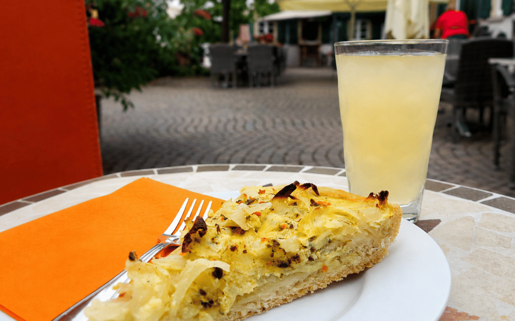 Zwiebelkuchen und Neuer Wein auf einem Tisch im Freien, umgeben von einer einladenden Atmosphäre.